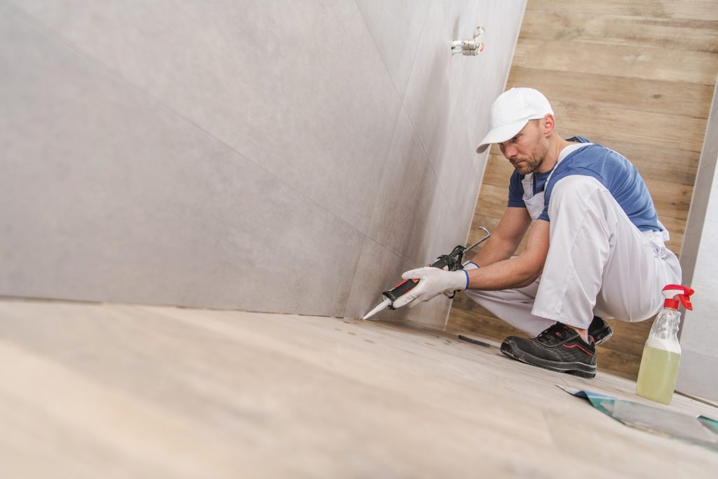 Caucasian Worker in His 30s Sealing Wall Corners of Ceramic Tiles Inside Newly Remodeled Bathroom. Using Silicone Sealant.